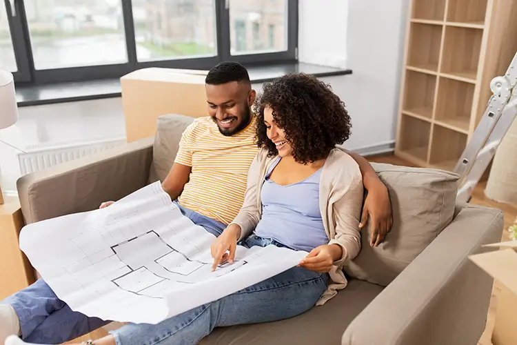 Young couple looking over blueprints for a house while sitting on a couch