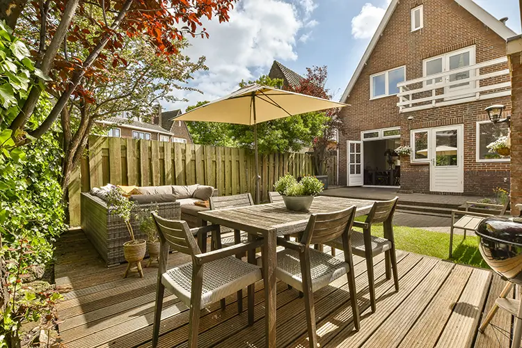 Patio with chairs and umbrella over a table in the backyard next to a brick house